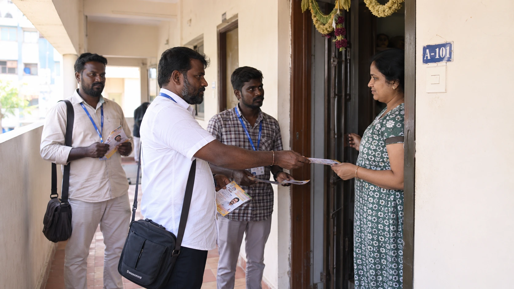 Campaign volunteers going door-to-door in a Chennai apartment complex corridor handing out pamphlets