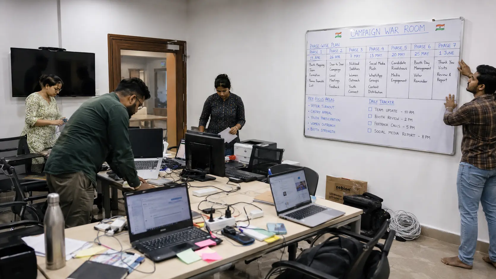 Team setting up an election war room, mounting a whiteboard with campaign phase timelines