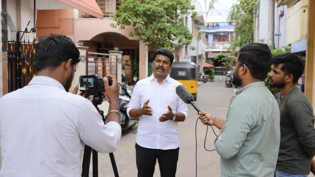 Candidate recording a Tamil YouTube campaign video on location in a Tamil Nadu neighbourhood with a small crew
